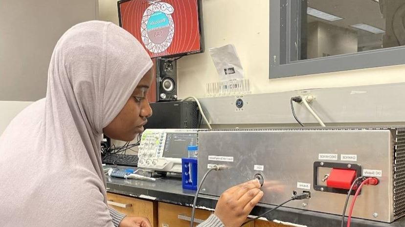 female lab student wearing a head covering adjusts lab equipment.